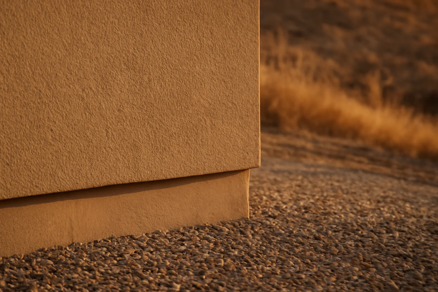 Stucco exterior wall meeting gravel ember-resistant zone near a wildland hillside